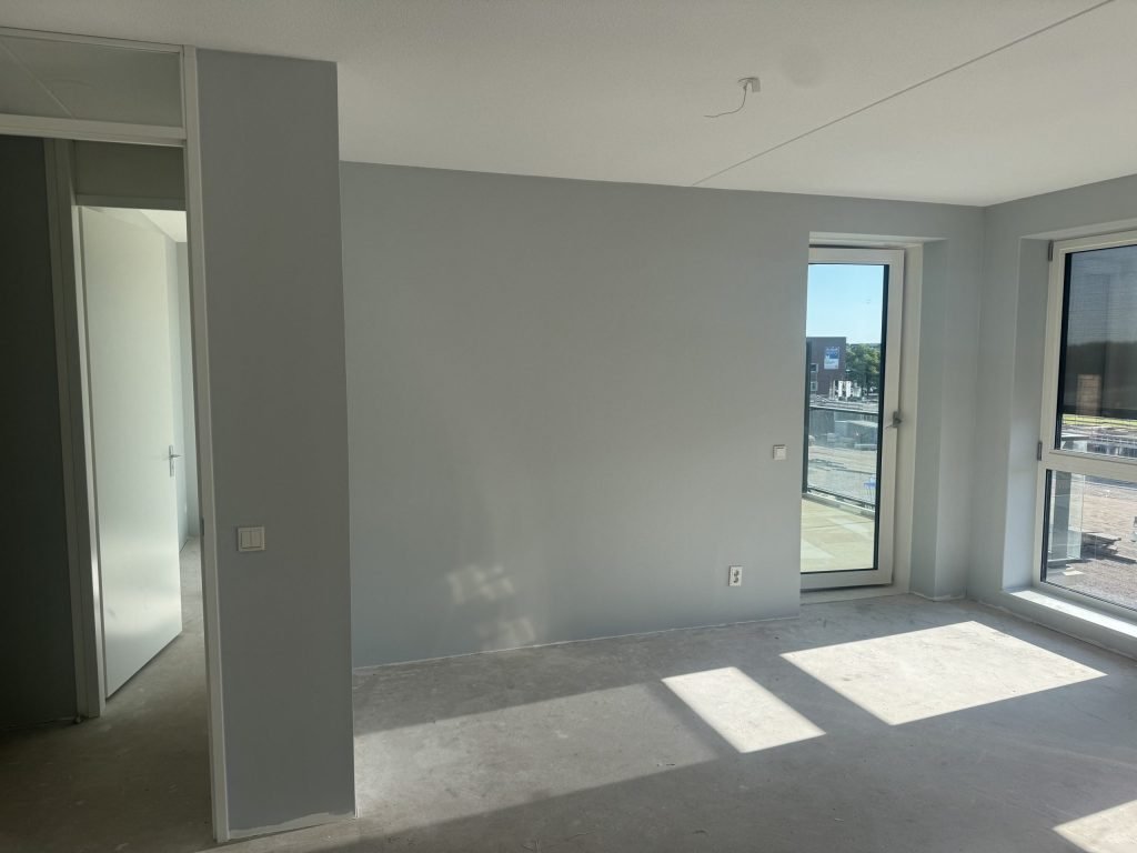 Lege nieuwbouwkamer met grijze wanden, een doorgang naar de gang en een betonvloer