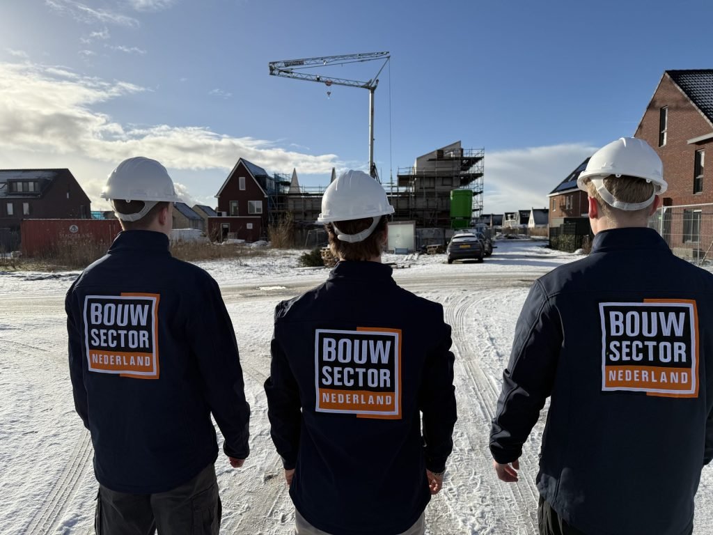 Drie vakmensen van achteren gezien met bedrijfsjas van Bouwsector Nederland voor een bouwkraan