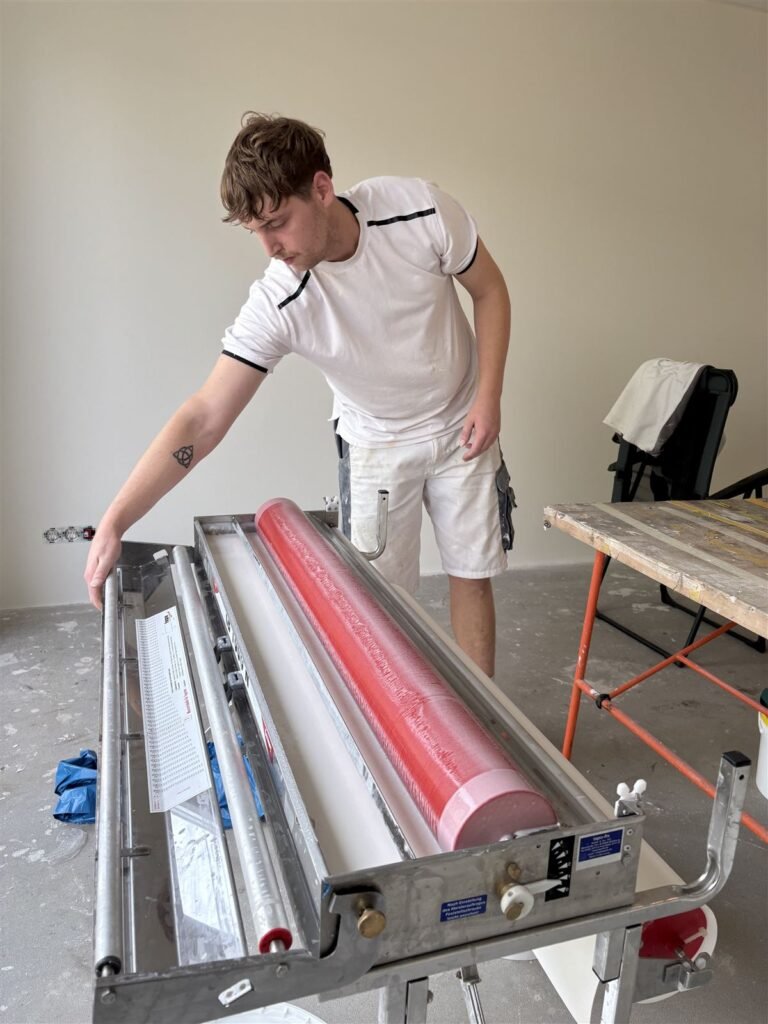 Behanger zet de inlijmmachine klaar om glasweefselbehang op maat te snijden en in te lijmen