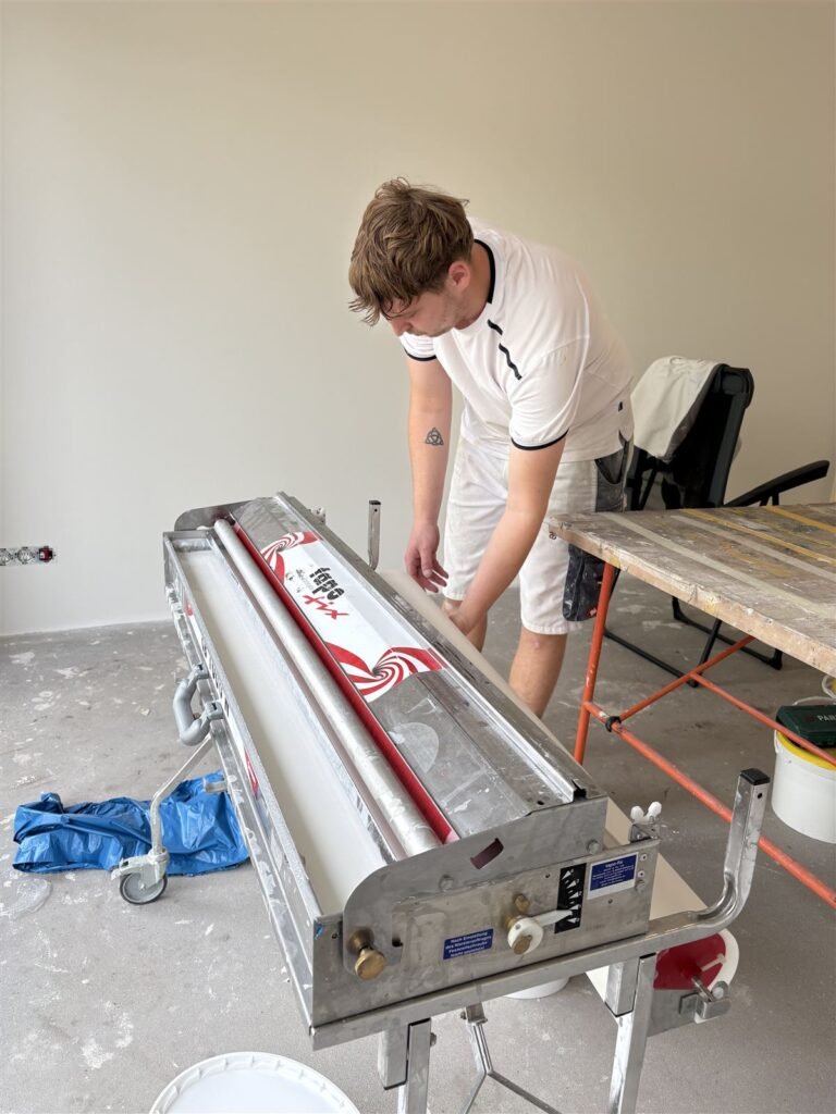 Behanger van Bouwsector Nederland aan de inlijmmachine voor glasweefselbehang