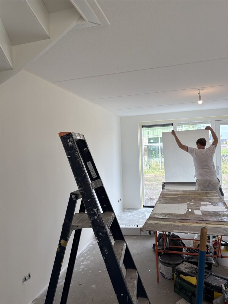 Behanger op de trap brengt een baan glasweefselbehang aan boven de schuifpui