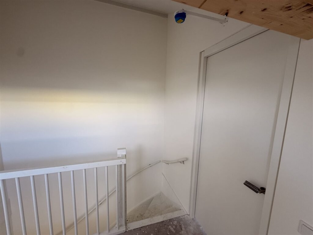 Gang boven in een nieuwbouwwoning met trapleuning en strak afgewerkte wand