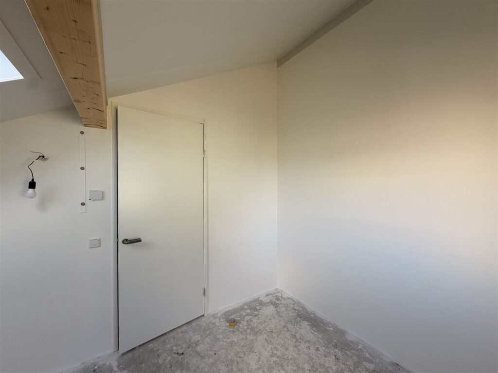 Kleine kamer onder de kap met deur en strak afgewerkte wanden