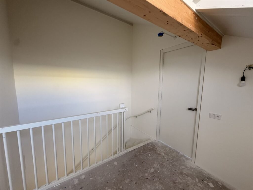 Overloop van een nieuwbouwwoning met trapleuning en afgewerkte wanden rond de deuren