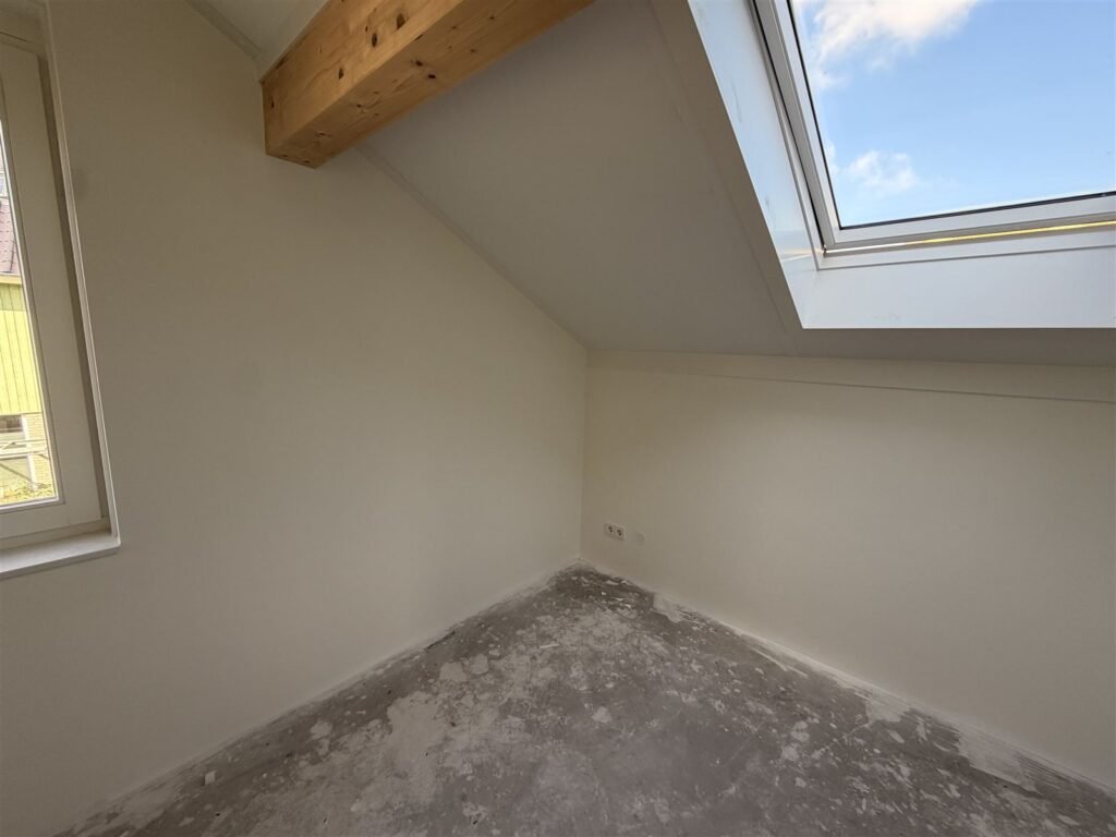 Zolderkamer met houten balk en dakraam na het behangen en sauzen