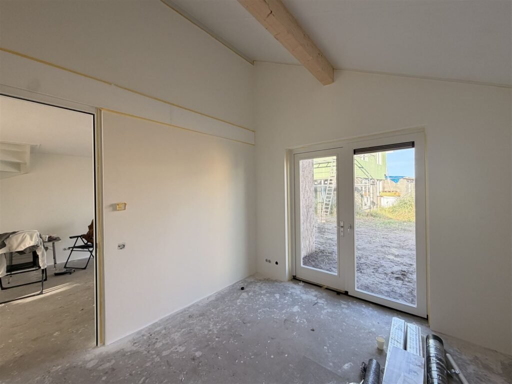 Afgewerkte nieuwbouwkamer met houten balk en tuindeuren, de wanden strak in het wit
